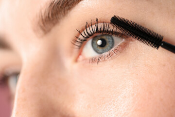 Young woman applying mascara onto her eyelashes, closeup