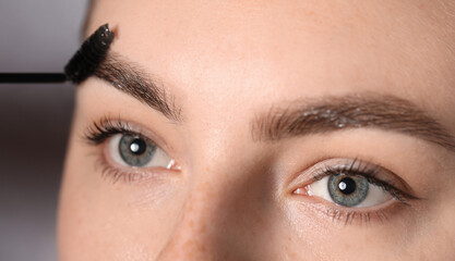 Naklejka premium Young woman brushing her eyebrow with spoolie on light grey background, closeup