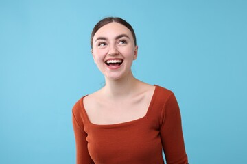 Beautiful woman laughing on light blue background. Positive emotion