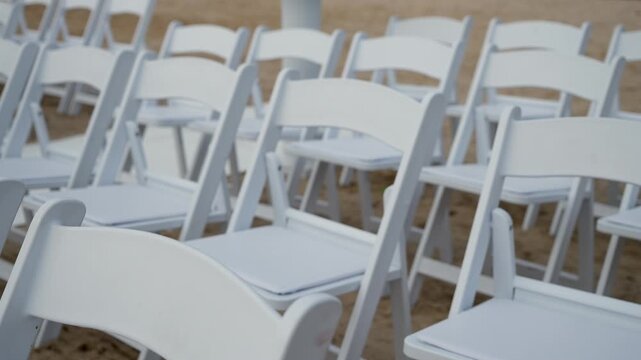 Elegant white chairs are arranged to create a stylish ambiance for a delightful outdoor event on sandy terrain