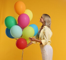 Happy woman with bunch of colorful balloons on yellow background