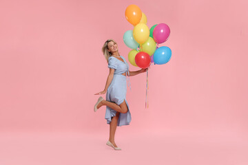 Smiling woman with bunch of colorful balloons on pink background