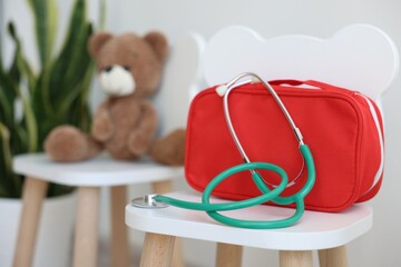 Pediatrician concept. Toy bear, medical bag and stethoscope on chairs in clinic, selective focus