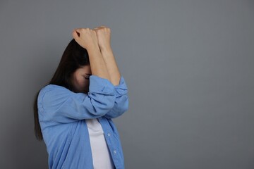 Woman suffering from panic attack on grey background, space for text