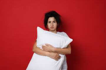 Woman with pillow suffering from hangover on red background