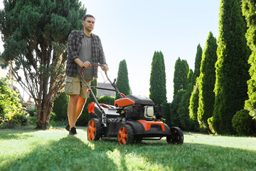 Man cutting green grass with lawn mower in garden, low angle view