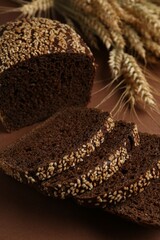 Fresh rye bread with seeds and spikes on brown background, closeup