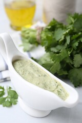 Tasty cilantro sauce in gravy boat on light table, closeup