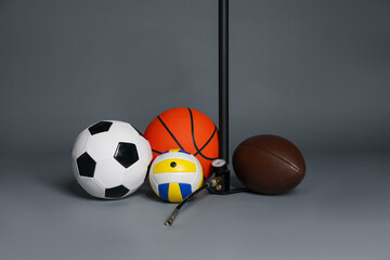 Different balls and manual air pump on grey background