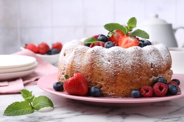 Tasty Bundt cake with powdered sugar and berries on white marble table, closeup