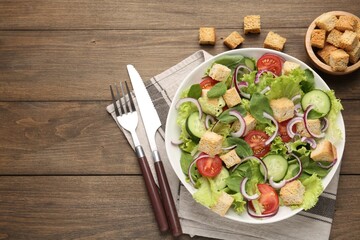 Delicious salad with croutons and vegetables on wooden table, flat lay. Space for text
