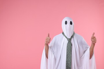 Man in ghost costume with tie showing thumbs up on pink background. Space for text