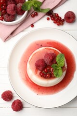 Delicious panna cotta with berries, sauce and mint on white wooden table, flat lay