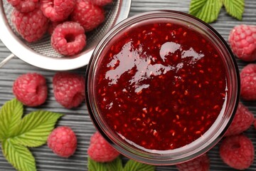 Sweet raspberry jam in glass jar and berries on dark gray wooden table, flat lay
