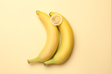 Sex education. Bananas with condom on beige background, flat lay