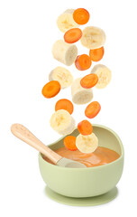 Baby food. Banana and carrot slices falling into bowl of puree on white background