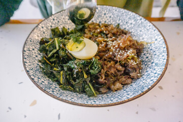 Beef teriyaki bowl with rice, egg, and fresh vegetables, with a woman's hands using chopsticks to eat. Delicious Japanese food