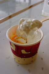 A creamy scoop of gelato is being eaten with a red spoon from a bright red cup, a vibrant and delicious summer dessert