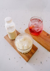 Refreshing strawberry squash and iced coffee latte on a rustic wooden coaster, perfect for a hot day. A delightful and vibrant beverage duo
