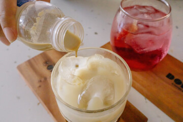 A captivating close-up of iced latte being poured into a glass, with a refreshing strawberry squash drink on the side