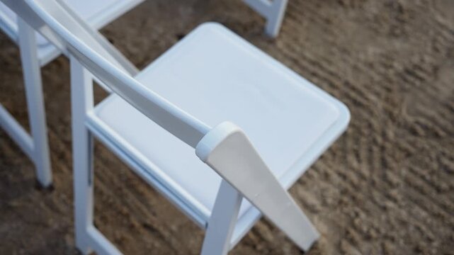 Elegant white chairs are arranged to create a stylish ambiance for a delightful outdoor event on sandy terrain