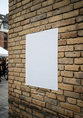 A blank white poster mockup glued to a textured tan brick wall on a city street.