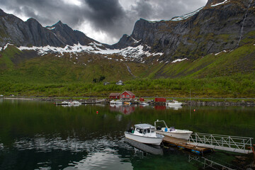 Calm Fjord With Boats And Red Huts In Front Of Snowy Mountains On Senja Island In Norway