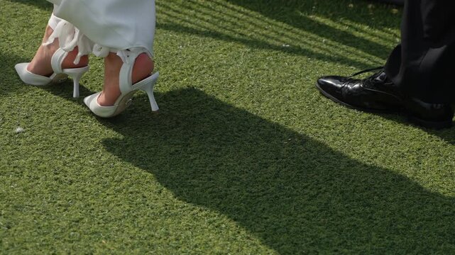 A detailed closeup of chic and stylish white high heels being elegantly worn on artificial grass at a wedding event