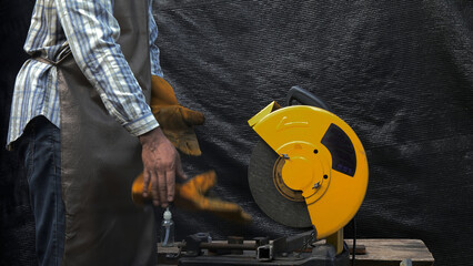 Worker standing beside yellow metal cutting saw wearing apron and gloves, preparing for or...