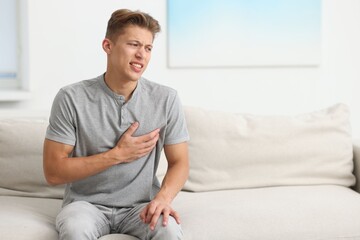 Young man suffering from chest pain on sofa at home. Space for text