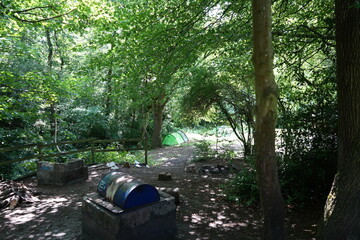 Woodland campsite with a tent and fire pit in the summer shade of Derbyshire, England.