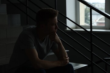 Sad thoughtful man sitting on stairs in darkness. Depression
