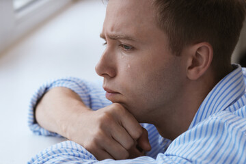Sad man crying alone indoors, closeup. Depression and anxiety