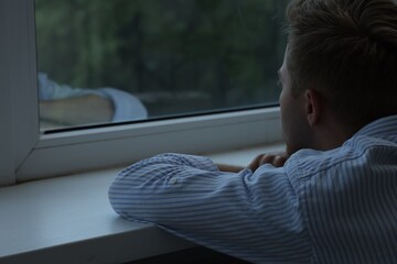 Sad lonely man looking at window indoors