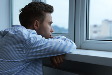 Sad lonely man looking at window indoors