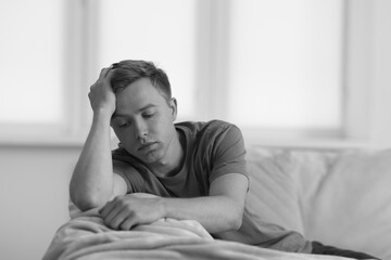 Sad thoughtful man on sofa at home, black and white effect