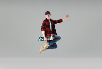 Happy young man with penny board jumping on light grey background