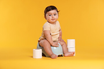 Cute little baby sitting on potty and rolls of toilet paper against orange background