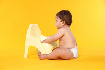 Cute little baby sitting near potty on orange background