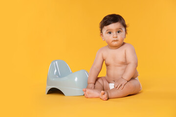 Cute little baby sitting near potty on orange background