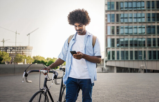African American man pushing bicycle while using on mobile phone app in the city