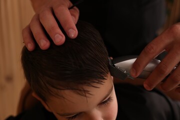 Professional barber working with little boy in barbershop, closeup