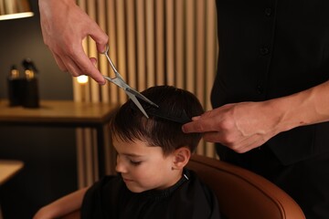 Professional barber cutting boy's hair in barbershop, closeup