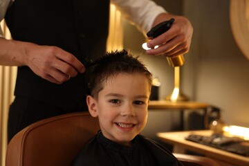 Professional barber working with little boy in barbershop, closeup