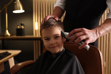 Professional barber working with little boy in barbershop, closeup