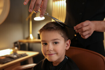 Professional barber cutting boy's hair in barbershop, closeup. Space for text