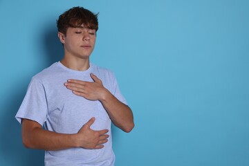 Teenage boy deep breathing on light blue background, space for text. Way to stop panic attack