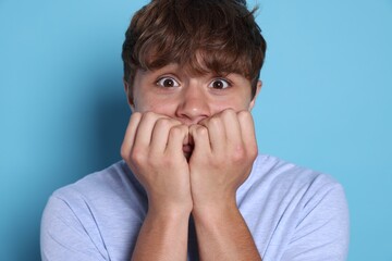 Teenage boy suffering from panic attack on light blue background