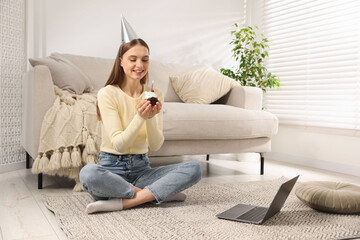 Obraz premium Birthday celebration. Happy woman with cupcake having video call via laptop at home