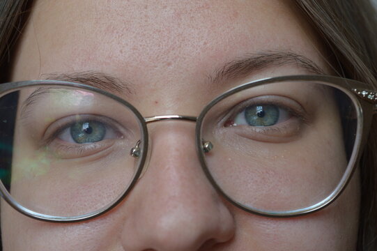 Close-up of blue eyes behind round glasses, showing detailed iris texture and skin. Perfect for eyewear ads, eye care promotions, or beauty and fashion campaigns.